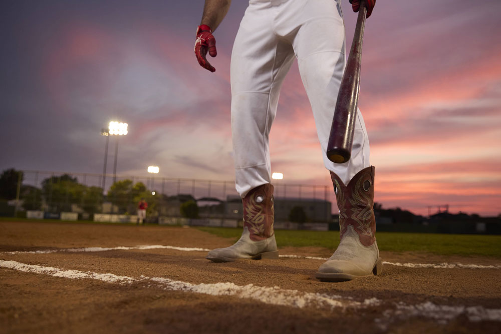 A man wearing Justin untamed western boots in red and grey while standing on a baseball field.